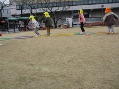 芝の上で2歳児がフラフープを並べてジャンプしている写真