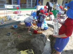 砂場で穴を掘ったり水を入れたりして遊んでいる写真