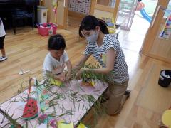 幼児が教師と一緒に笹に七夕飾りを飾っている写真