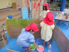 絵の具コーナーで段ボールの囲いに色を塗る幼児の写真