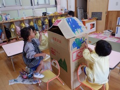 絵の具で段ボールハウスに色を塗る幼児の写真