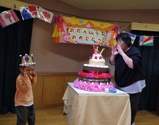 誕生会で大きなケーキのろうそくを消す幼児と先生
