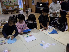 魚に絵を描く幼児たちと見守る中学生