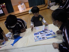 魚に絵を描く幼児と見守る中学生
