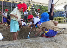 小学生と一緒に砂場で穴を掘る