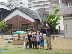 保育士と芝生に水やりをする子どもの写真