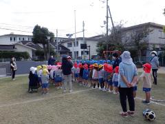 芝生に並んで避難訓練で園長先生の話を聞いている幼児の写真