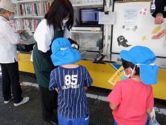 移動図書館の係員に借りる本を見せている幼児の写真