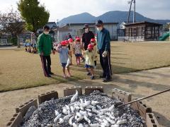 焼き芋を薪に投入する幼児の写真