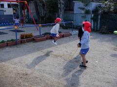 園庭で友達と長縄跳びをしている幼児の写真