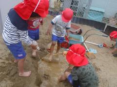 年中児が裸足で真砂土山で穴を掘って水をためて遊んでいる写真