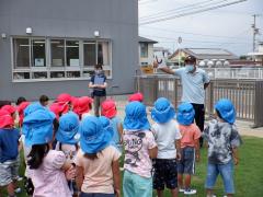 火災の避難訓練で子どもたちが芝生に集まり先生の話を聞いている写真