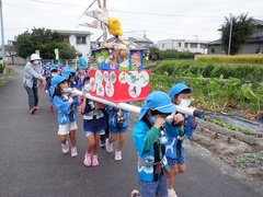 おみこしパレードで手作りみこしを担ぐ幼児の写真