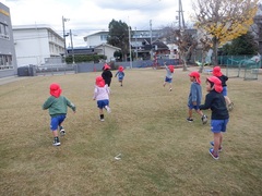 戸外で鬼ごっこをして遊んでいる幼児の写真