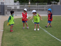 芝生でリレーごっこをする幼児の写真