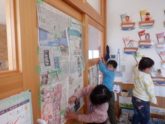 保育室の窓に新聞紙を貼って秘密の活動をしようとする幼児の写真