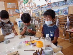 ドングリを使って飾りを作っている幼児の写真