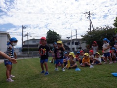 芝生園庭でリレーごっこをする幼児の写真