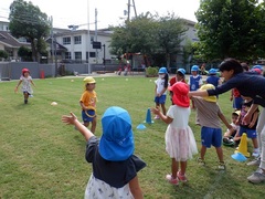 芝生園庭でリレーごっこをする幼児の写真