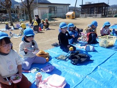 芝生園庭でお弁当を食べる幼児の写真