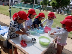 洗面器を使って泡を作って遊ぶ幼児の写真