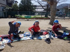 芝生園庭でお弁当を食べる幼児の写真