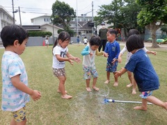 スプリンクラーで水遊びをする幼児の写真