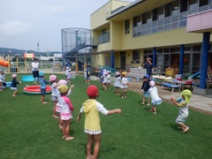 芝生園庭で水遊びの前の体操をする幼児の写真