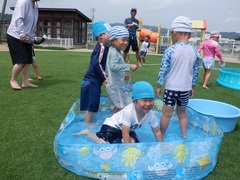 芝生園庭で水遊びをする幼児の写真