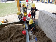 砂場でトイに水を流して遊んでいる幼児の写真