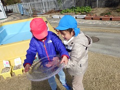 大きな丸の氷を持つ幼児と、下から手をかざす幼児