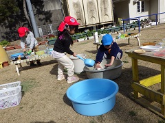 ひしゃくを使ってタライに水を入れる幼児