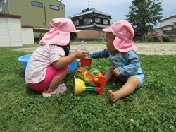 0歳児と2歳児が芝生の上で水遊びを楽しんでいる写真