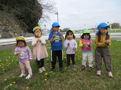 子どもたちがたんぽぽの綿毛を吹いて飛ばしている写真