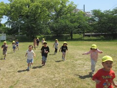 芝生の広場でかけっこをする子どもたちの写真