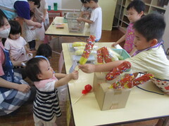夏祭りごっこで5歳児が0歳児に製作したチョコバナナを渡している写真