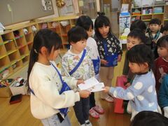 5歳児が３歳児に年賀状を渡している写真