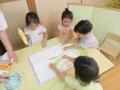自分たちで剥いたトウモロコシの皮を画用紙に貼って造形遊びを楽しんでいる写真